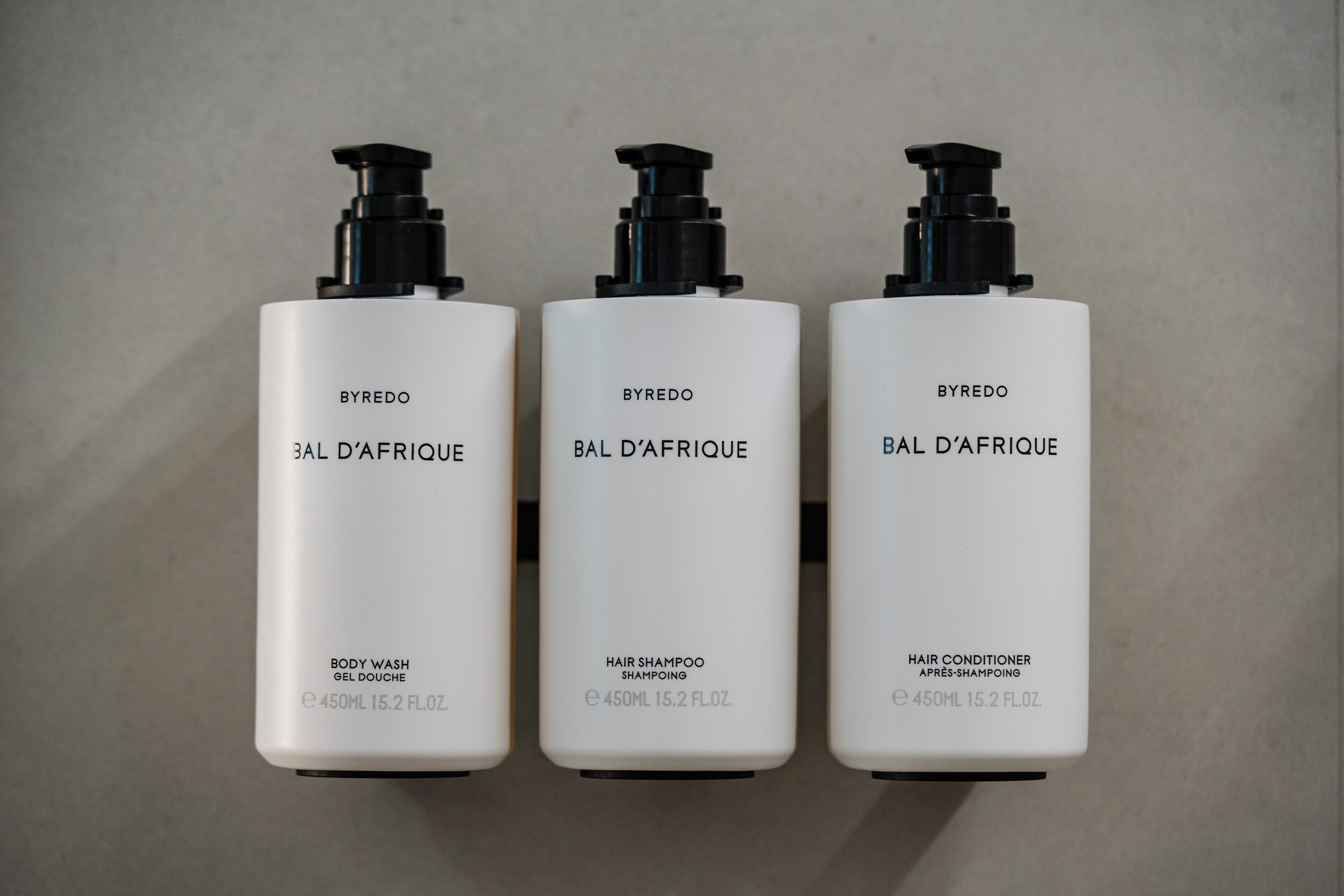 Three white bottles of BYREDO BAL D'AERIQUE body wash, hair shampoo, and hair conditioner, each with a black pump dispenser.