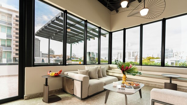 A modern living room with a sofa, a coffee table, and a small side table. There is a large window providing a view of the cityscape. - Magdalena 1163 (San Juan)