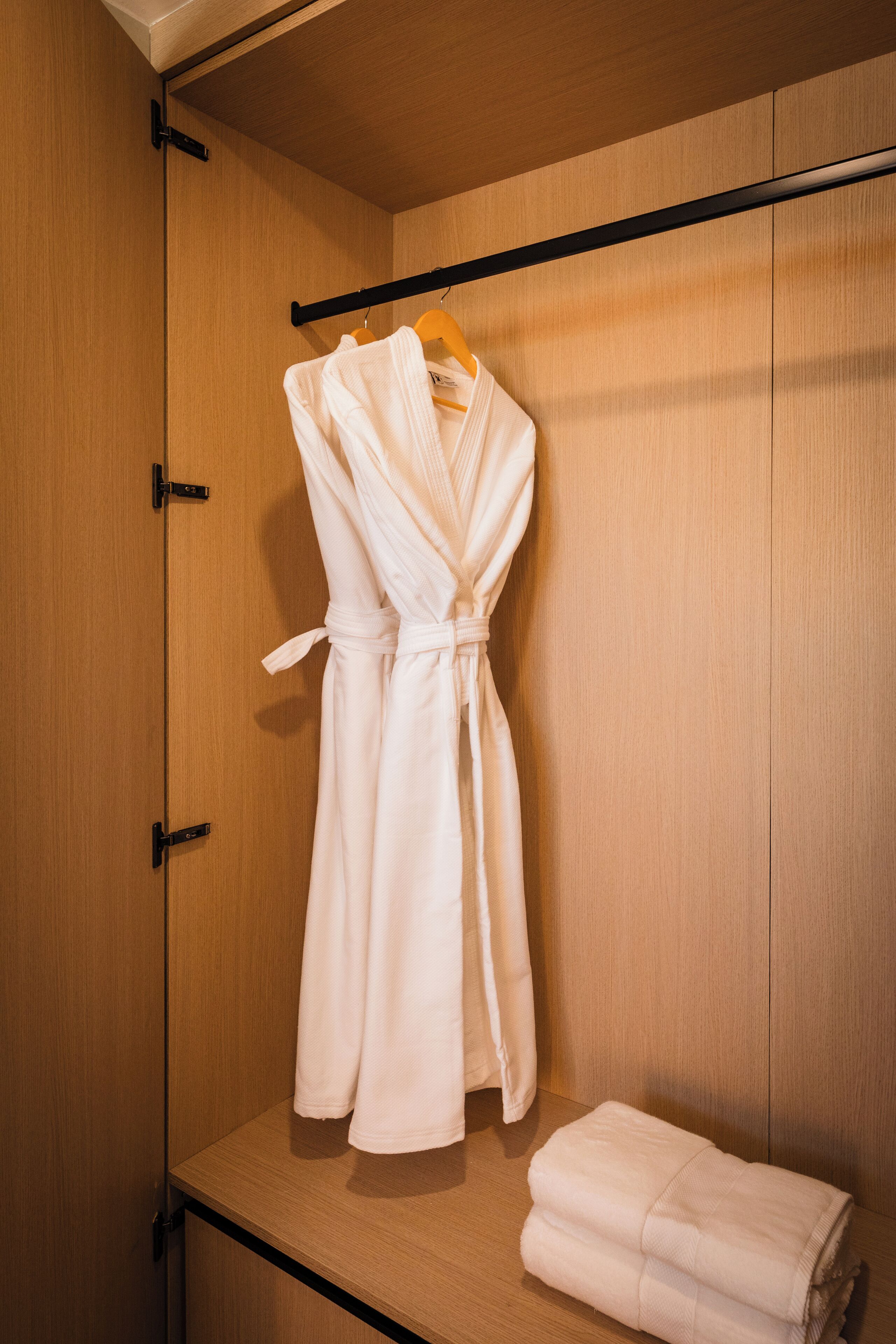 A wooden wardrobe with a robe hanging on a rod and a folded towel on the shelf.