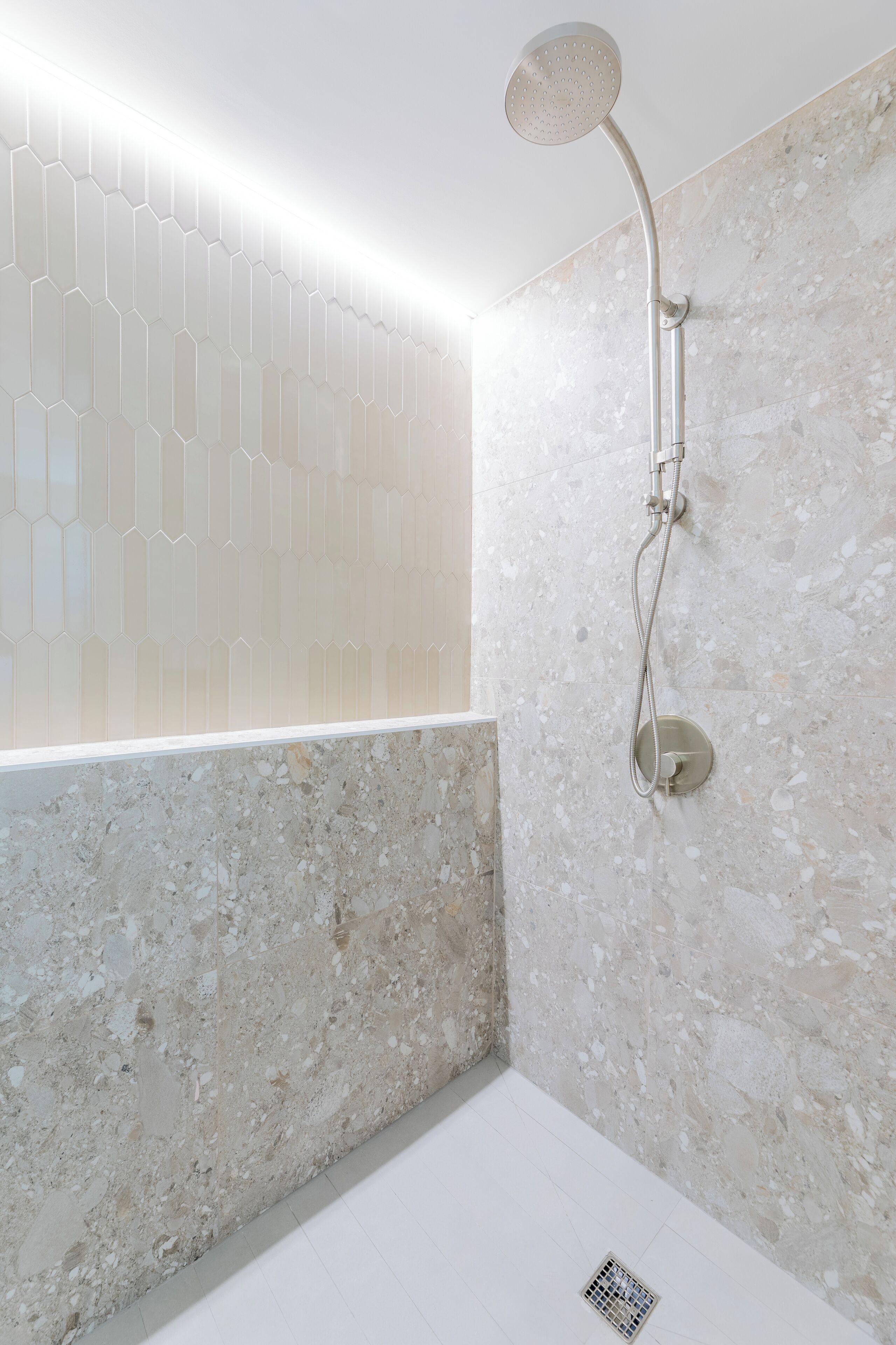 Un baño moderno con ducha, pared de azulejos hexagonales y pared de piedra veteada.