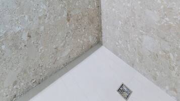 Un baño moderno con ducha, pared de azulejos hexagonales y pared de piedra veteada.