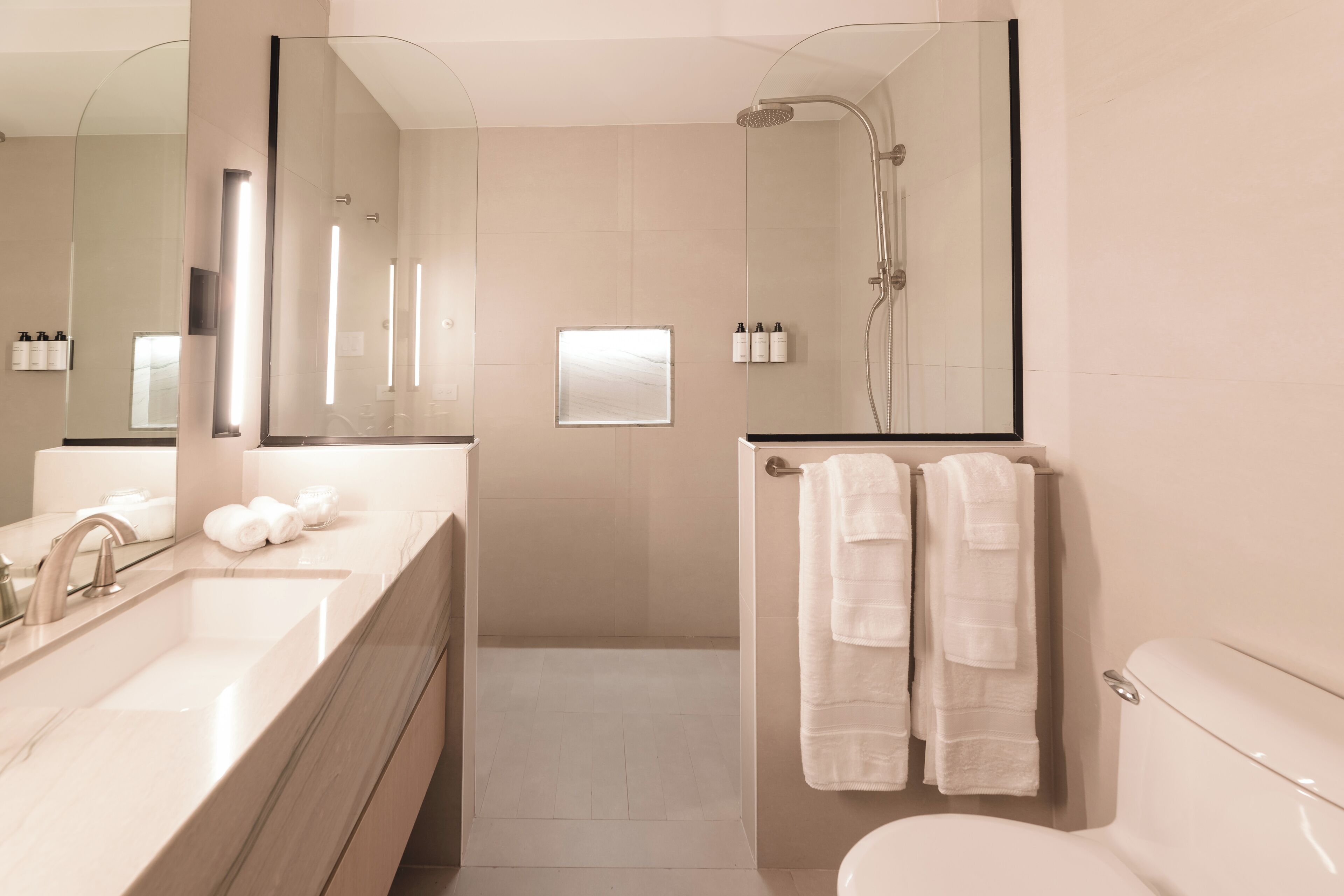 Un baño moderno con un espejo grande, un lavabo, una ducha y un inodoro.