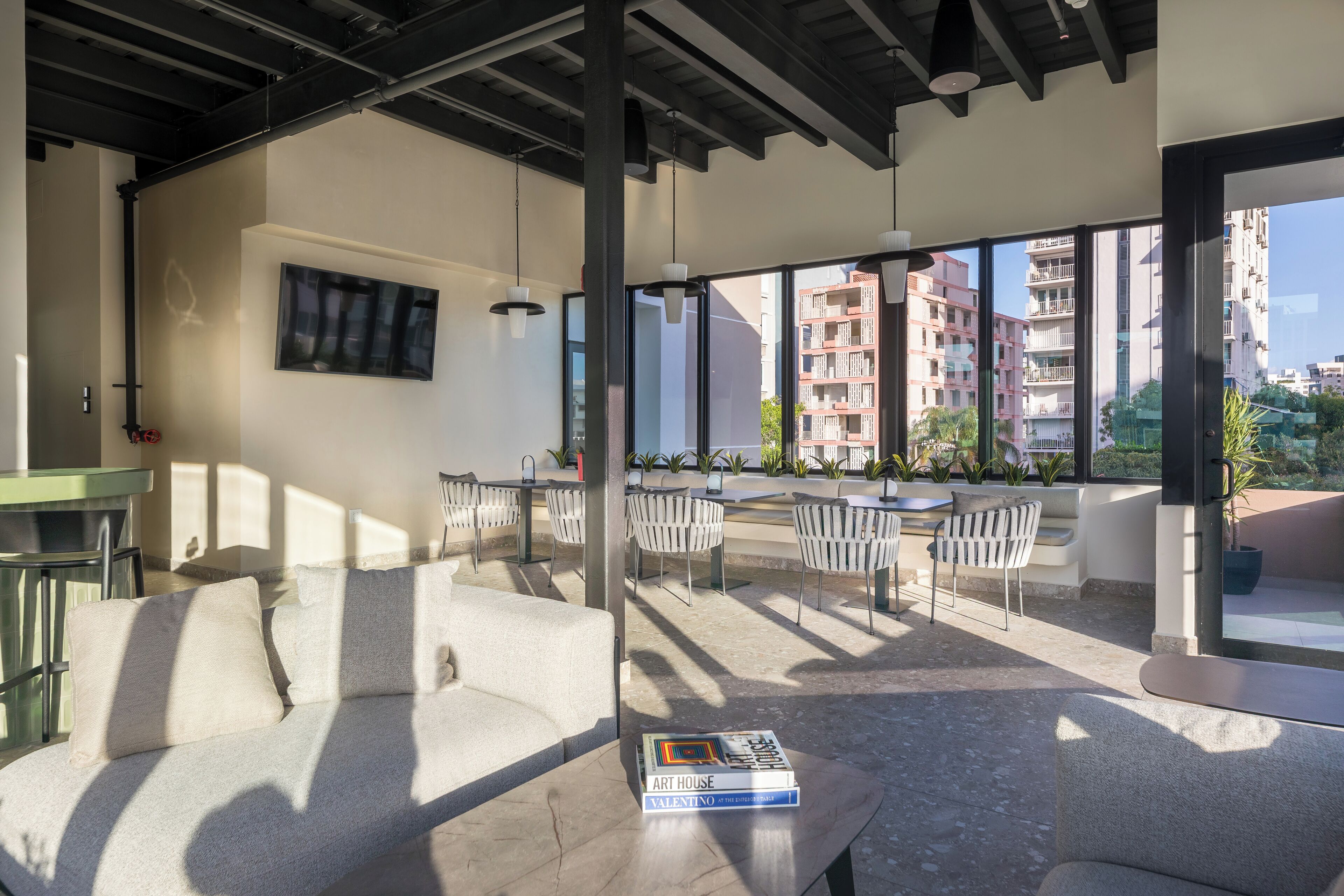 A modern living area with a sofa, dining table, and chairs, large windows with a city view, and a book on the table.