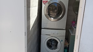 Un lavadero con dos lavadoras apiladas, una cuenca azul en la parte superior y un armario pequeño con dispensador de agua.