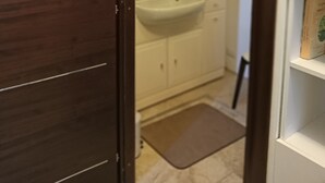 Un baño con puerta de madera, un lavamanos blanco, un espejo y una repisa con un libro.