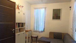 Una sala de estar con un sofá, una mesita, una estantería y una ventana con cortinas de encaje.