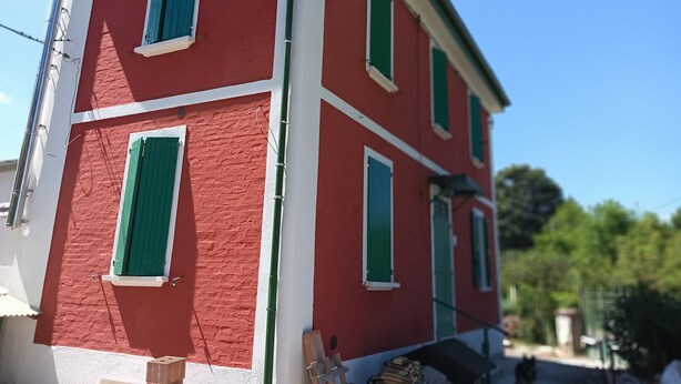 Un edificio rojo con contraventanas verdes y detalles blancos.