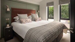 A bedroom with a large bed, a nightstand, a window with a view of greenery, and a skylight. - Wansfell, Whitbarrow (Penrith)