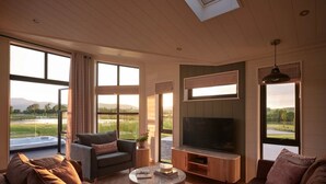 A spacious living room with a large flat-screen TV, comfortable seating, and large windows offering a view of the outdoors. - Wansfell, Whitbarrow (Penrith)