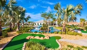 Een golfbaan met een putting green, een zwembad en palmbomen.