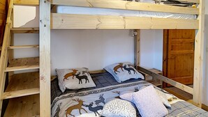 En våningssäng med en trästege, två kuddar med djurmönster och en mönstrad filt.