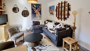 Ett modernt vardagsrum med en soffa, ett runt soffbord, en tv och dekorativa föremål på väggarna.