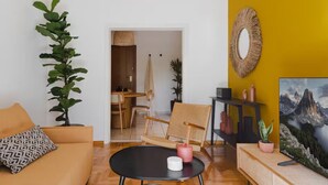Un soggiorno con divano, tavolino, zona pranzo con sedie, una parete colorata di giallo e un quadro.