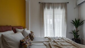 Una camera da letto con un letto, cuscini, una coperta, una finestra con tende e una pianta in vaso.