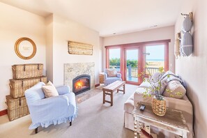 Ein gemütliches Wohnzimmer mit Kamin, Korbwannen, gestreifter Möbel und Blick auf den Strand durch große Schiebetüren.