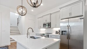 A modern kitchen with white cabinetry, stainless steel appliances, a central island with a sink, and a chandelier. - King-bed home near East Nashville with easy access to local attractions (Nashville)