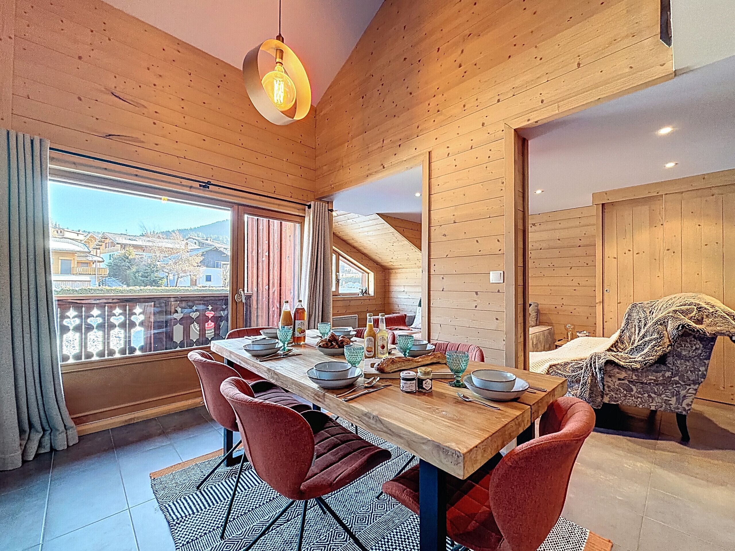A dining area with a wooden table, red chairs, and a view of the outside.