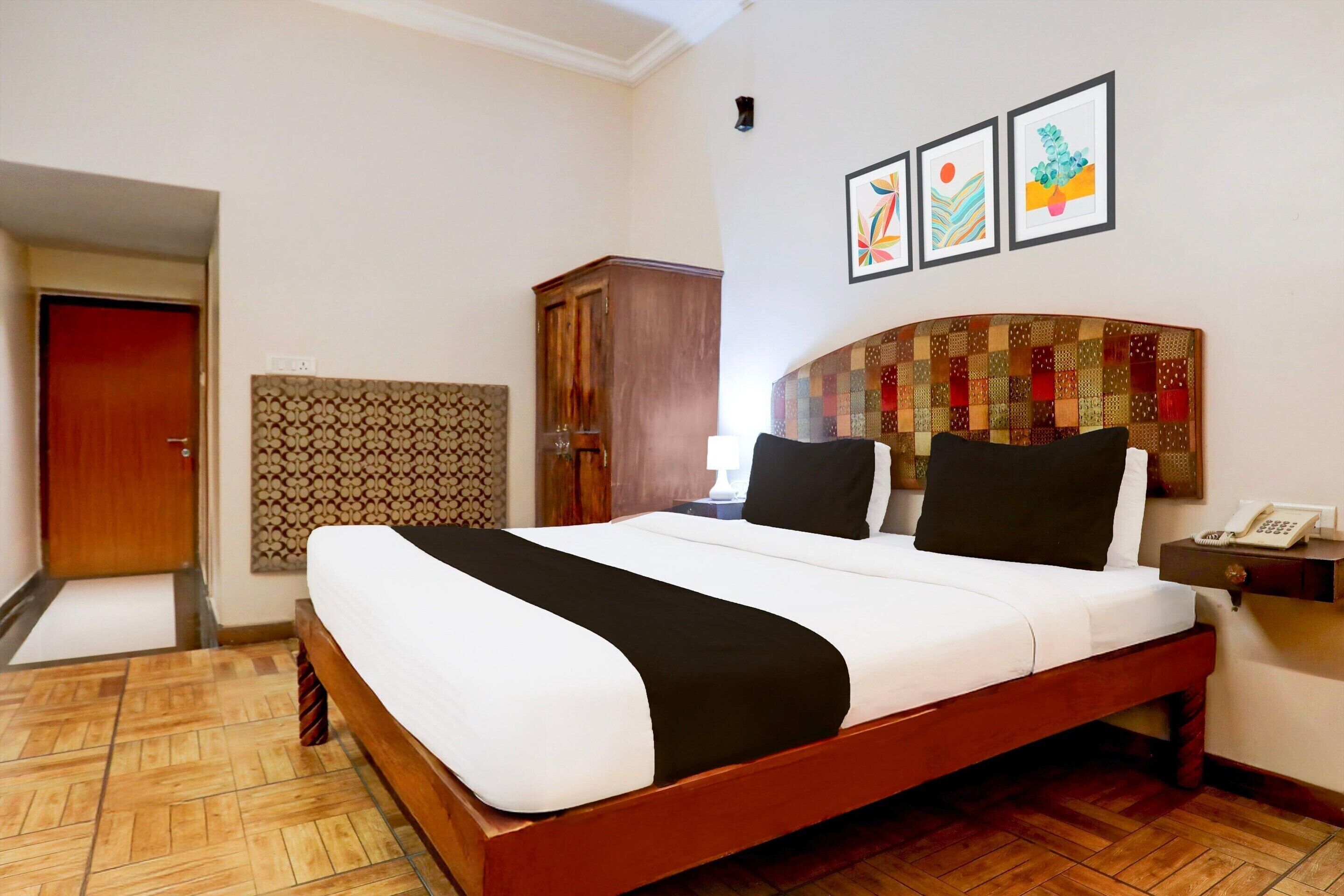 Habitación de hotel con una cama grande, cabecera de madera, un armario y una mesita de noche pequeña con un teléfono.