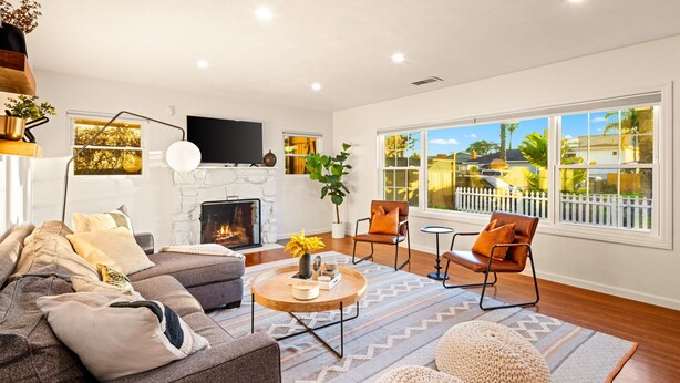 A living room with a fireplace, a sofa, a coffee table, and a view of a fenced yard. - Mins To Beach W/ Jacuzzi, Large Yard,Parking & AC! (Oceanside)