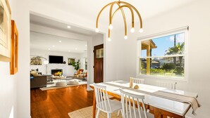 A spacious living area with a dining table, white chairs, a fireplace, and a large window with a view. - Mins To Beach W/ Jacuzzi, Large Yard,Parking & AC! (Oceanside)