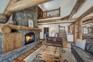 Un intérieur rustique avec une cheminée en pierre, des poutres en bois, un canapé et un escalier menant à un niveau supérieur.