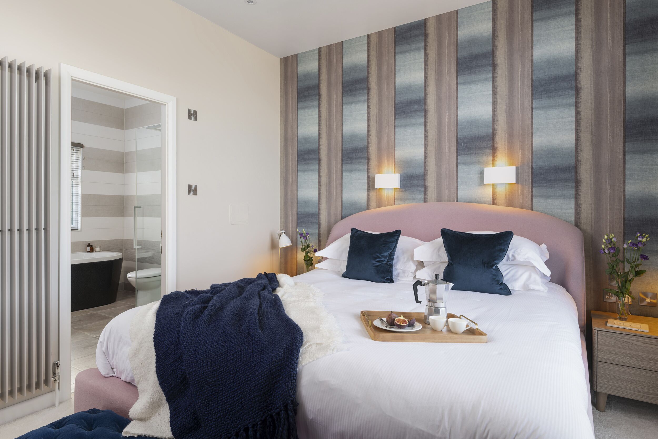 Ett modernt hotellrum med en stor säng, sänglampor, ett nattduksbord och utsikt över badrummet.