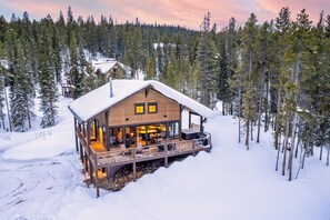 A wooden cabin with a deck, surrounded by snow-covered trees.