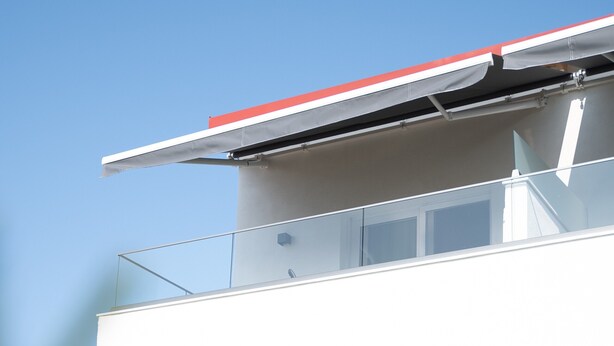 Un edificio moderno con techo plano, un balcón con barandilla de vidrio y una puerta de madera.