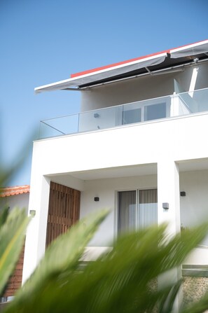 Un bâtiment moderne doté d’un toit plat, d’un balcon avec des garde-corps en verre et d’une porte en bois.