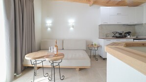 Una habitación moderna con sofá, dos mesitas, una zona de cocina y techo de madera.