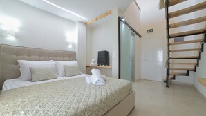 Un dormitorio con cama, mesita de noche, maleta, toalla, escalera de madera y una puerta.