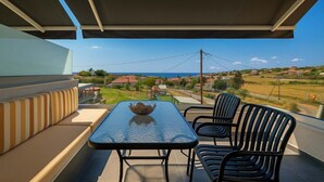 Un balcon avec une table et des chaises, un saladier posé sur la table, et une vue sur les maisons et la mer.