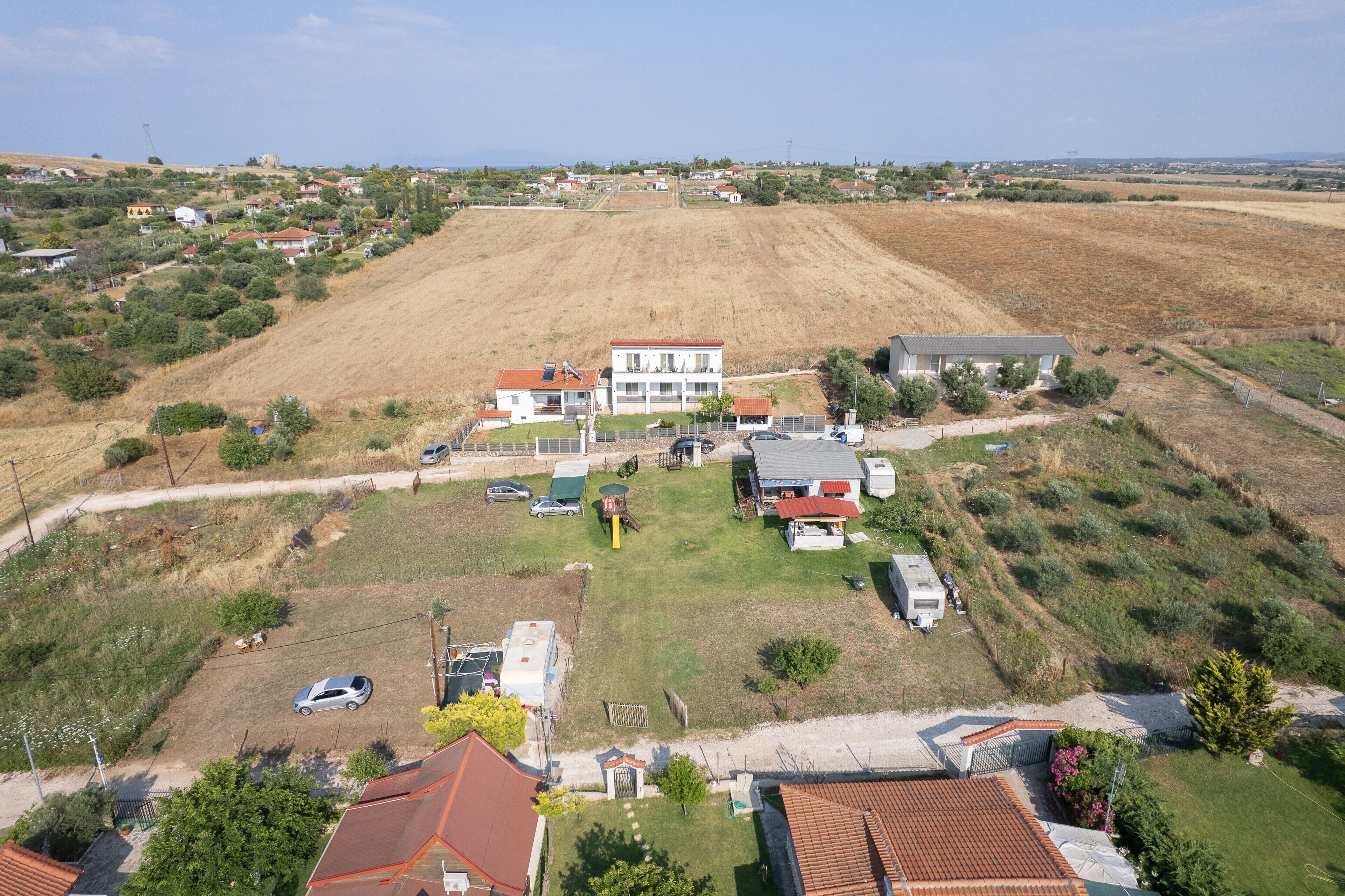 An aerial view of a residential area with houses, a grassy field, and a parked caravan.