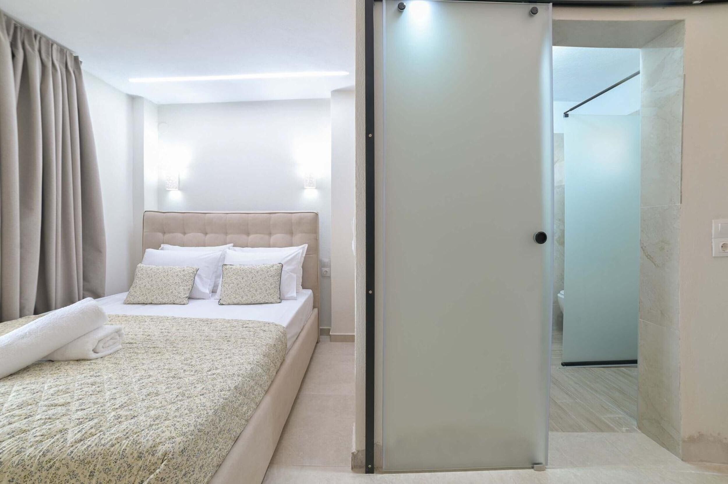A hotel room with a bed, a bedside table, a wall-mounted light, and a sliding door leading to a bathroom.