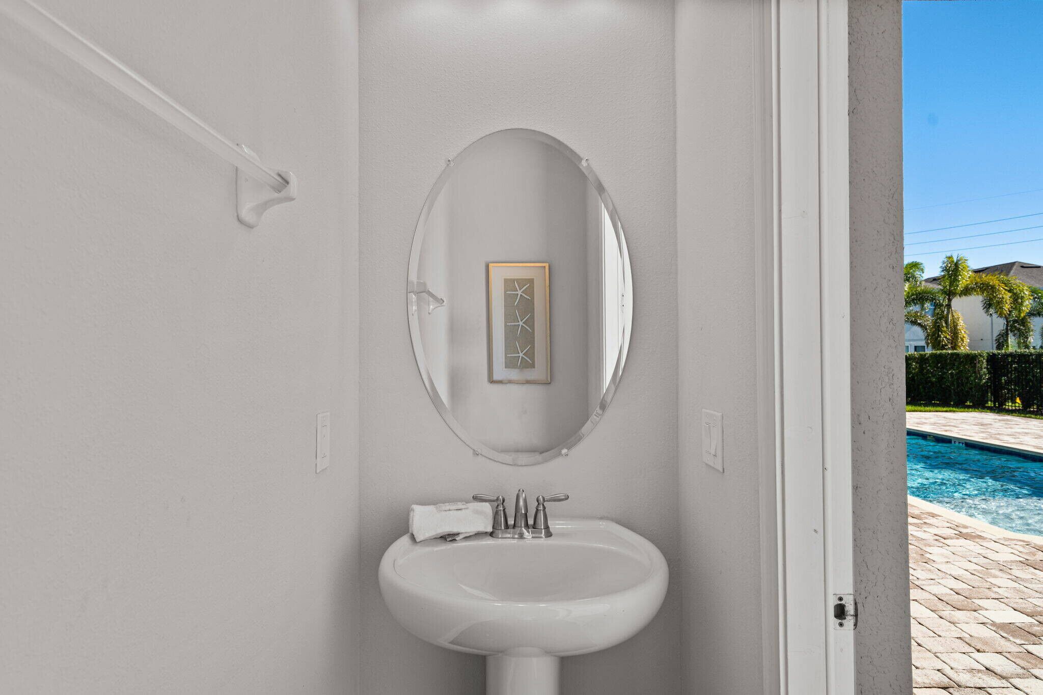 A bathroom with a white sink, a mirror, and a framed artwork above it.