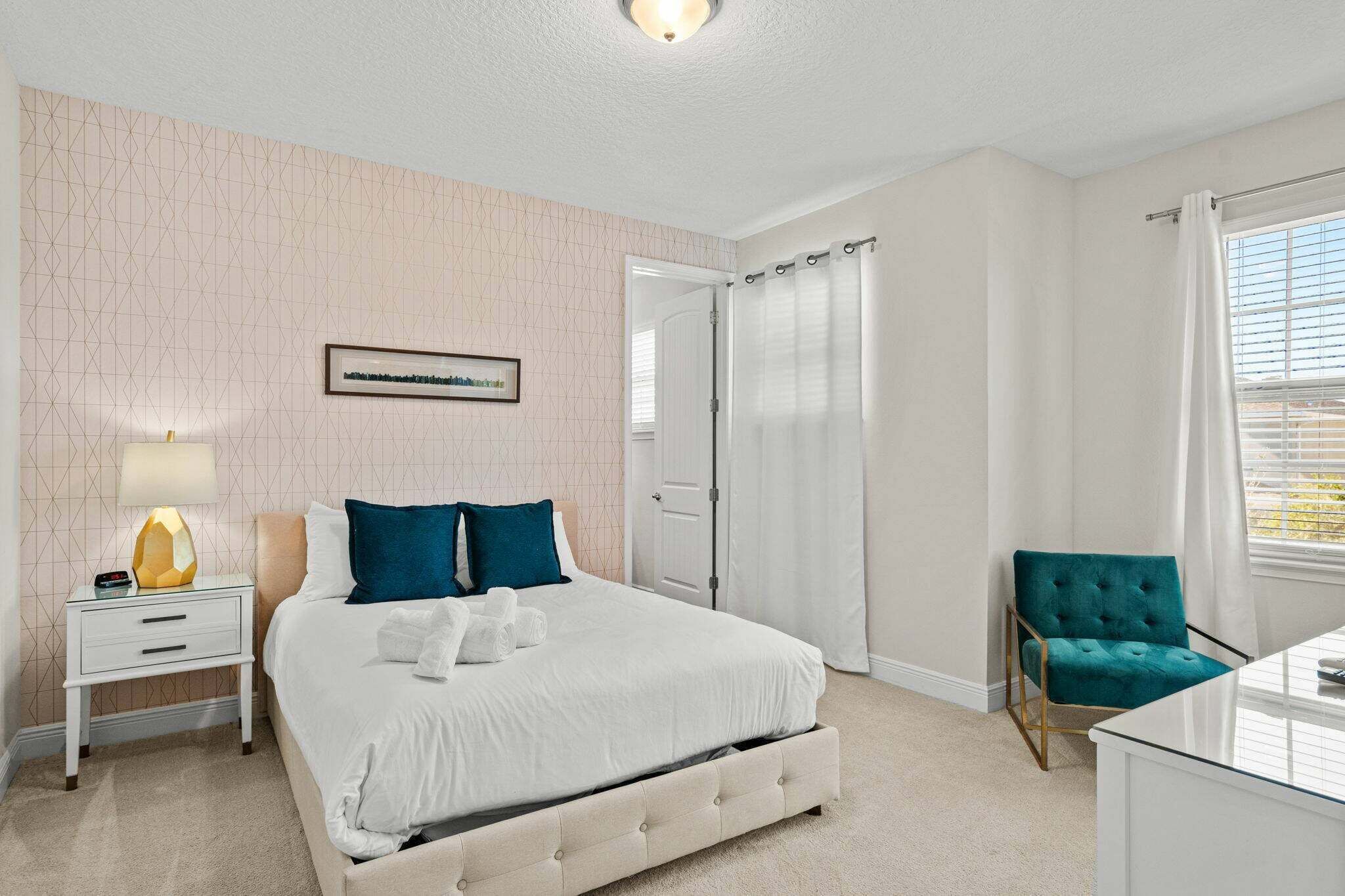 Un dormitorio con cama, mesita de noche, silla y un cuadro en la pared.