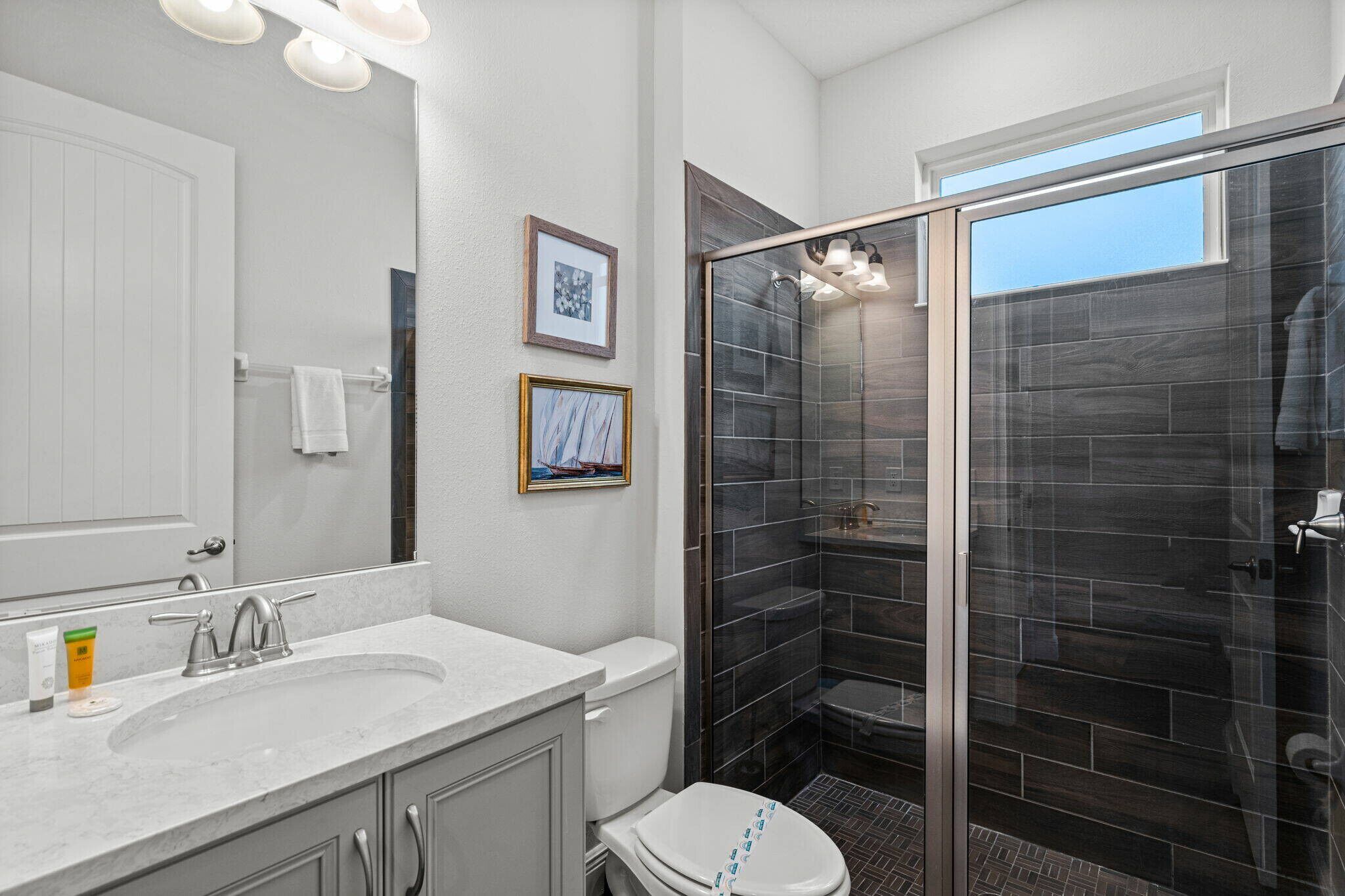 A modern bathroom with a white vanity, a glass shower enclosure, and two framed pictures on the wall.