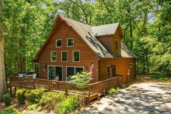 A wooden cabin with a deck, surrounded by dense forest. - Peaceful Lake Keowee Home, Quiet Cove in Serenity Bay, Great for Clemson Events (Seneca)