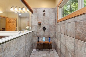 A shower with stone tiles, a wooden shelf with toiletries, and a window with a view of trees. - Peaceful Lake Keowee Home, Quiet Cove in Serenity Bay, Great for Clemson Events (Seneca)