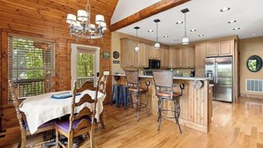Un intérieur en bois comprenant une table à manger, des chaises, un coin bar et une cuisine avec des meubles en bois et des appareils en acier inoxydable.