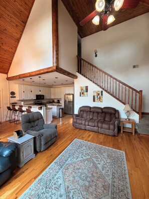 A spacious living area with a high ceiling, a wooden staircase, and a kitchen in the background. - Peaceful Lake Keowee Home, Quiet Cove in Serenity Bay, Great for Clemson Events (Seneca)