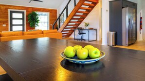 Een moderne keuken met een houten trap, een eettafel met een schaal groene appels en een koelkast.
