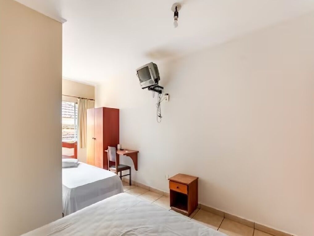 A hotel room with two beds, a desk, a chair, and a TV mounted on the wall.