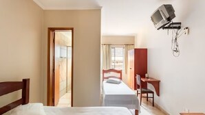 A hotel room with a bed, a desk, a chair, and a television mounted on the wall. - Agrishow 2026 - Quarto Single e Duplo  (Ribeirão Preto)