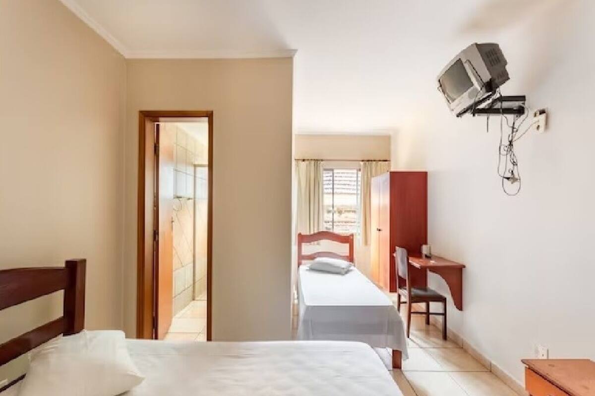 A hotel room with a bed, a desk, a chair, and a television mounted on the wall.