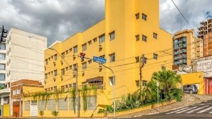 A yellow building with multiple windows and balconies, a street sign, and a clear sky. - Agrishow 2026 - Quarto Single e Duplo  (Ribeirão Preto)