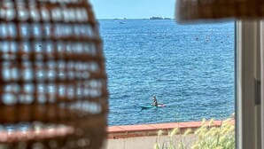 Vista a través de una ventana con una persiana de mimbre, una masa de agua y una costa lejana.