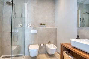 A modern bathroom with a glass-enclosed shower, a toilet, a bidet, and a large sink with a wooden vanity. - House on the Seafront in Calella – Iconic “Casa Rosa” (Calella de Palafrugell)