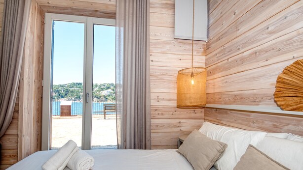 Un dormitorio con cama, cortinas, una lámpara colgante y vistas a través de un ventanal.