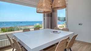 Un comedor con una mesa grande, sillas de mimbre y vistas al mar.